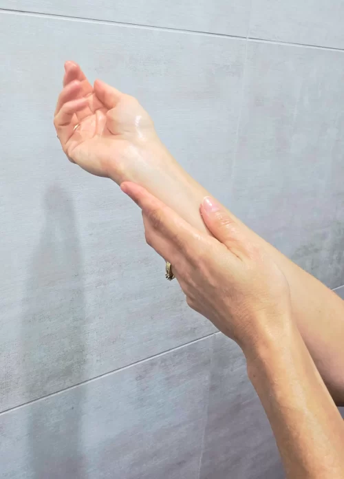 a light skinned arm glistening with oil and other hand massaging arm