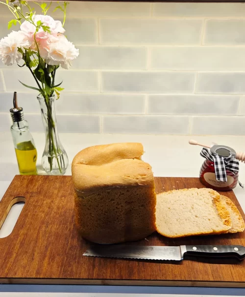 A freshly baked loaf of bread sits on a cutting board with a knife placed next to it.